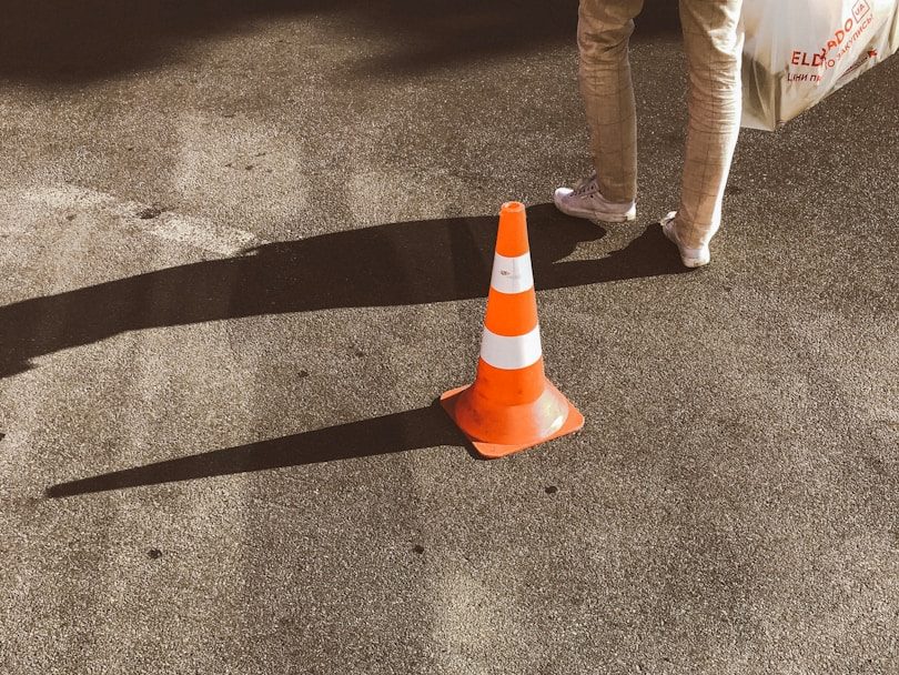 Más de accidentes de trabajo Cono de tráfico naranja con blanco en una superficie pavimentada, sombra visible.